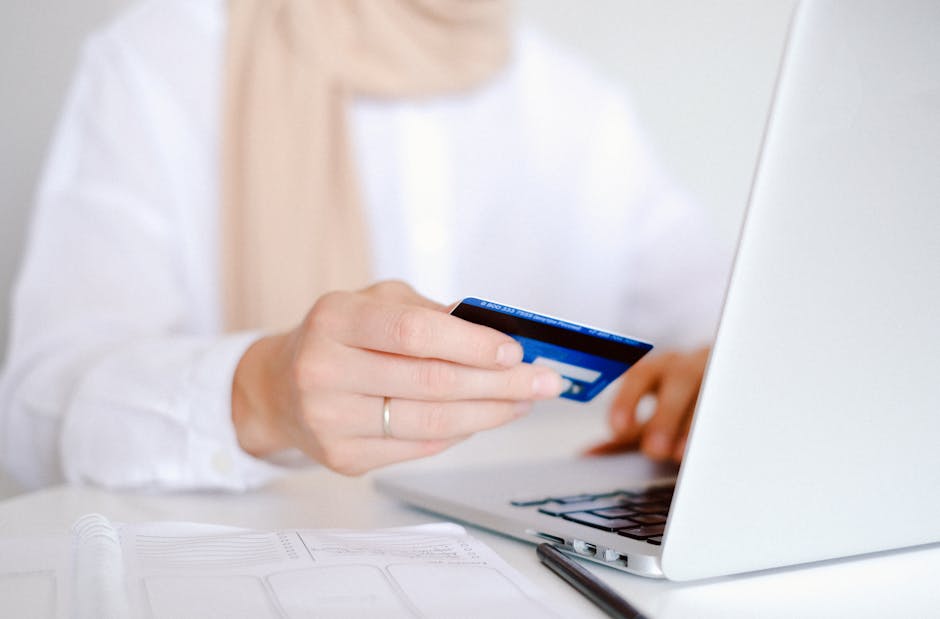 Close-up of a person holding a credit card while using a laptop for online shopping.